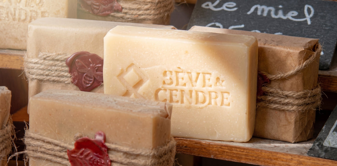 Savon SAF solide au lait de chèvre posé sur un support en bois entourés d'autres savons Sève et Cendre