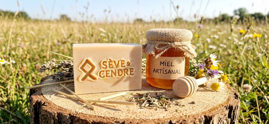 Savon au miel artisanal gravé posé sur une buche de bois brute à côté d'un pot de miel